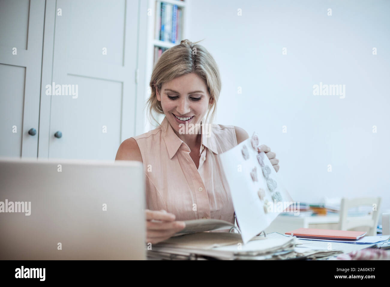 Donna sorridente con notebook lavorando sul design di moda su tavola Foto Stock
