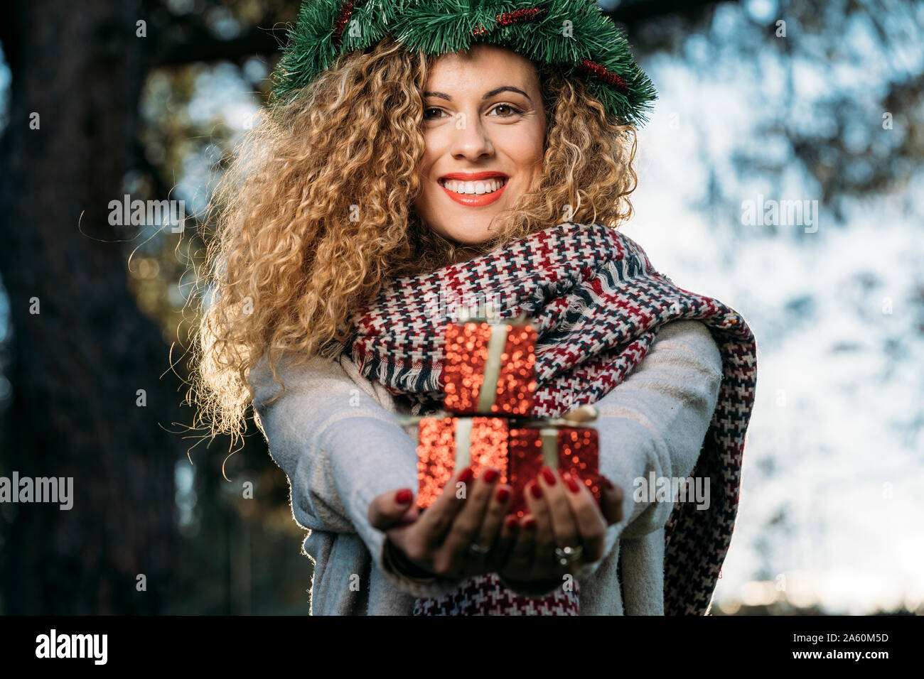 Ritratto di sorridente giovane donna con la ghirlanda di Natale sul suo capo la presentazione di regalo di Natale Foto Stock