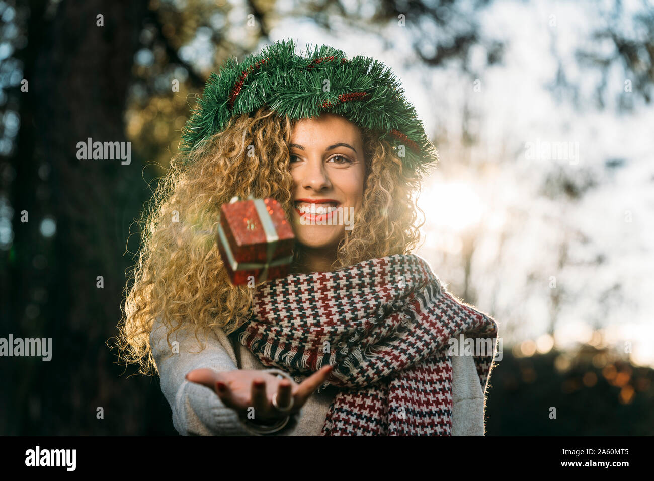 Ritratto di sorridente giovane donna con la ghirlanda di Natale sul suo capo la giocoleria con il regalo di Natale Foto Stock
