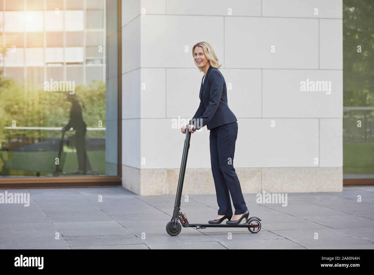 Imprenditrice sull'e-scooter passando edificio per uffici in città Foto Stock