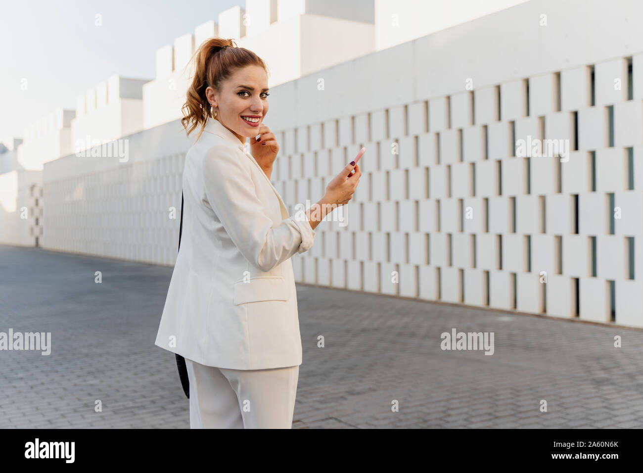 Imprenditrice in bianco pant suit, utilizza lo smartphone Foto Stock