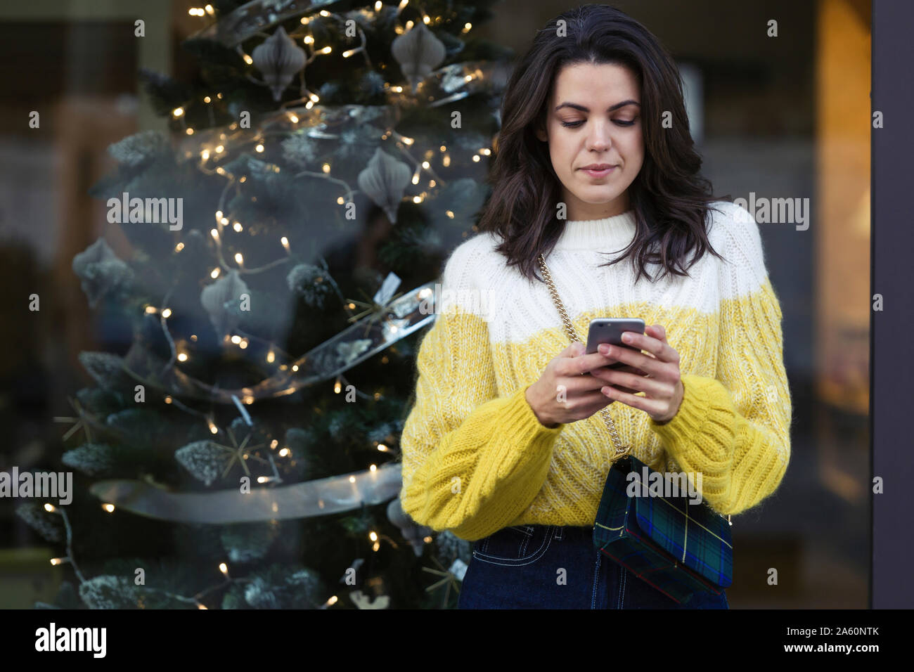 Piuttosto giovane donna che usa il suo smartphone davanti alla vetrina di un negozio nella città Foto Stock