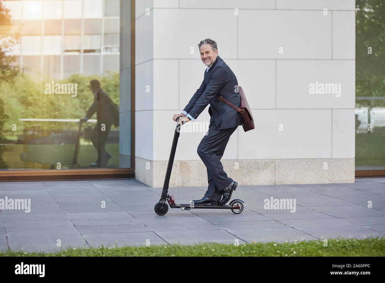 Imprenditore su e-scooter passando edificio per uffici in città Foto Stock