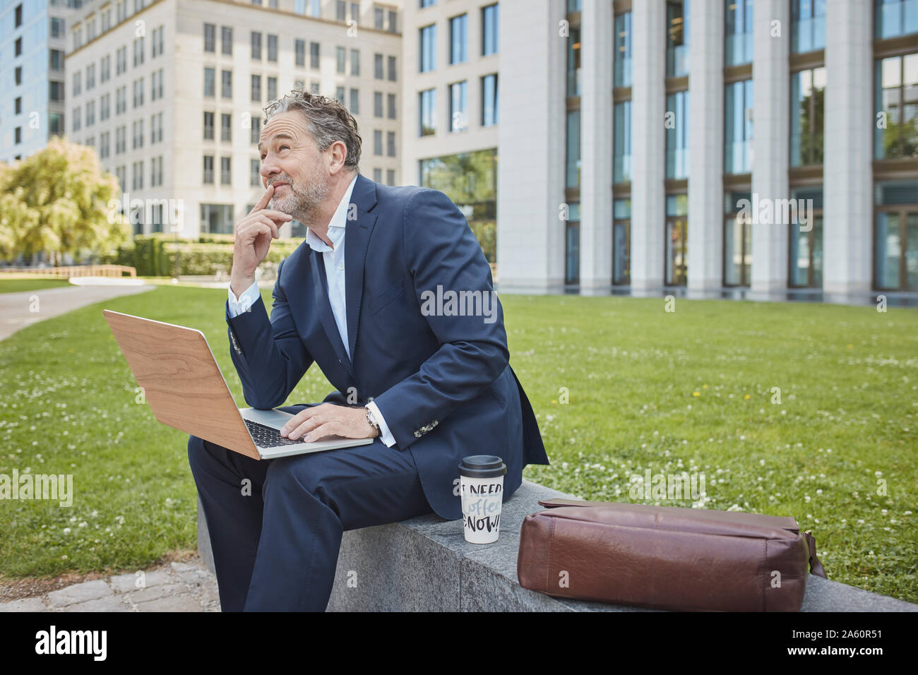 Imprenditore maturo seduto su di una parete della città utilizzando laptop Foto Stock