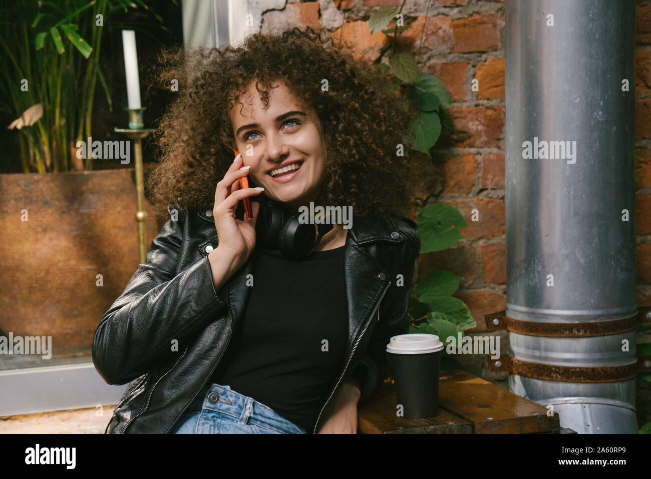 Ritratto di felice ragazza adolescente al telefono seduta a outdoor cafe con caffè per andare Foto Stock