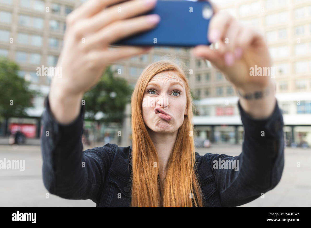 Ritratto di redheaded giovane donna busbana francese bocca tenendo selfie con lo smartphone, Berlino, Germania Foto Stock