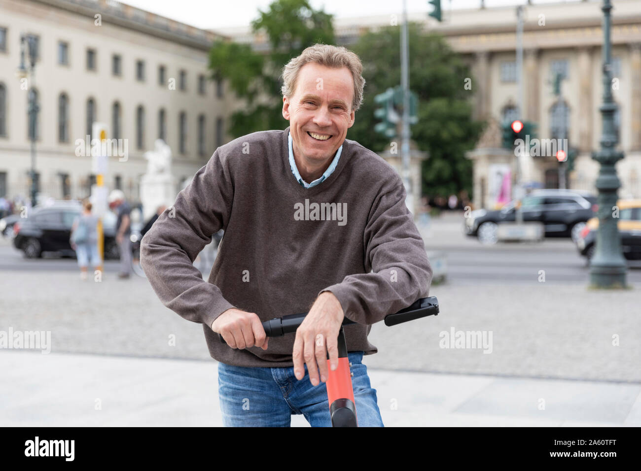 Ritratto di felice senior uomo appoggiato su scooter elettrico nella città di Berlino, Germania Foto Stock