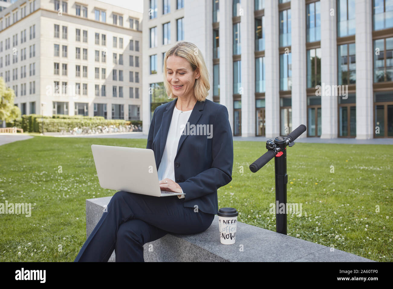 Imprenditrice seduta su di una parete della città utilizzando laptop Foto Stock