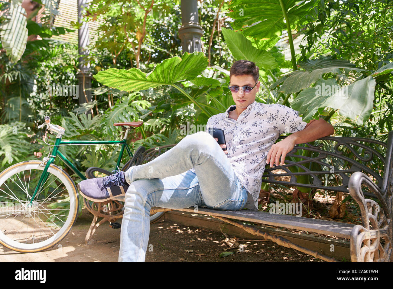 Uomo con bicicletta seduta su una panchina in un parco che usa il suo smartphone Foto Stock