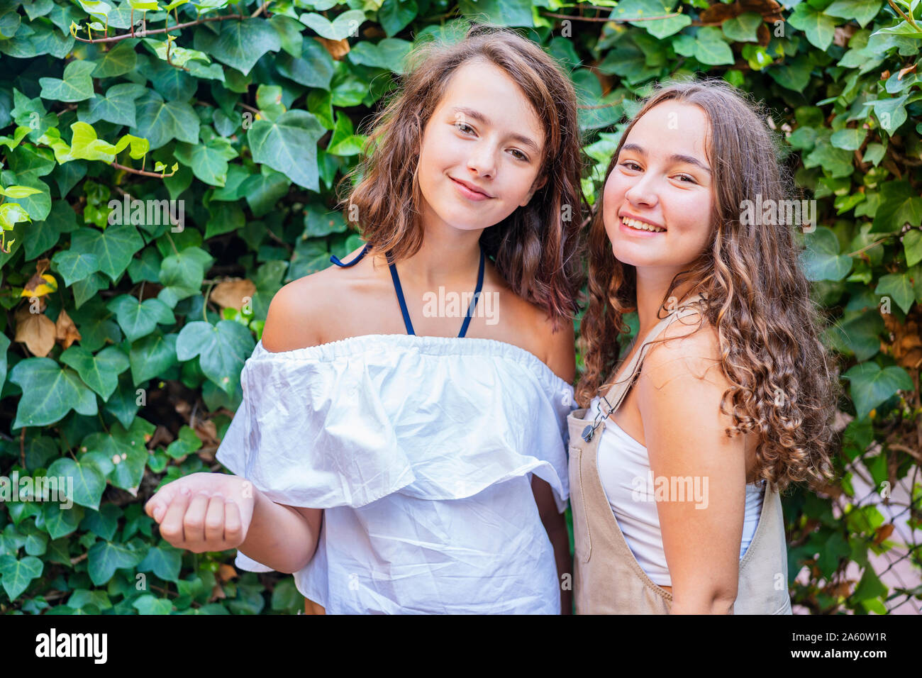 Le giovani ragazze cercando di fotocamera a sorridere su sfondo di edera Foto Stock