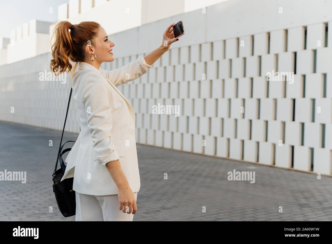 Imprenditrice in bianco pant suit, tenendo selfie dello smartphone Foto Stock
