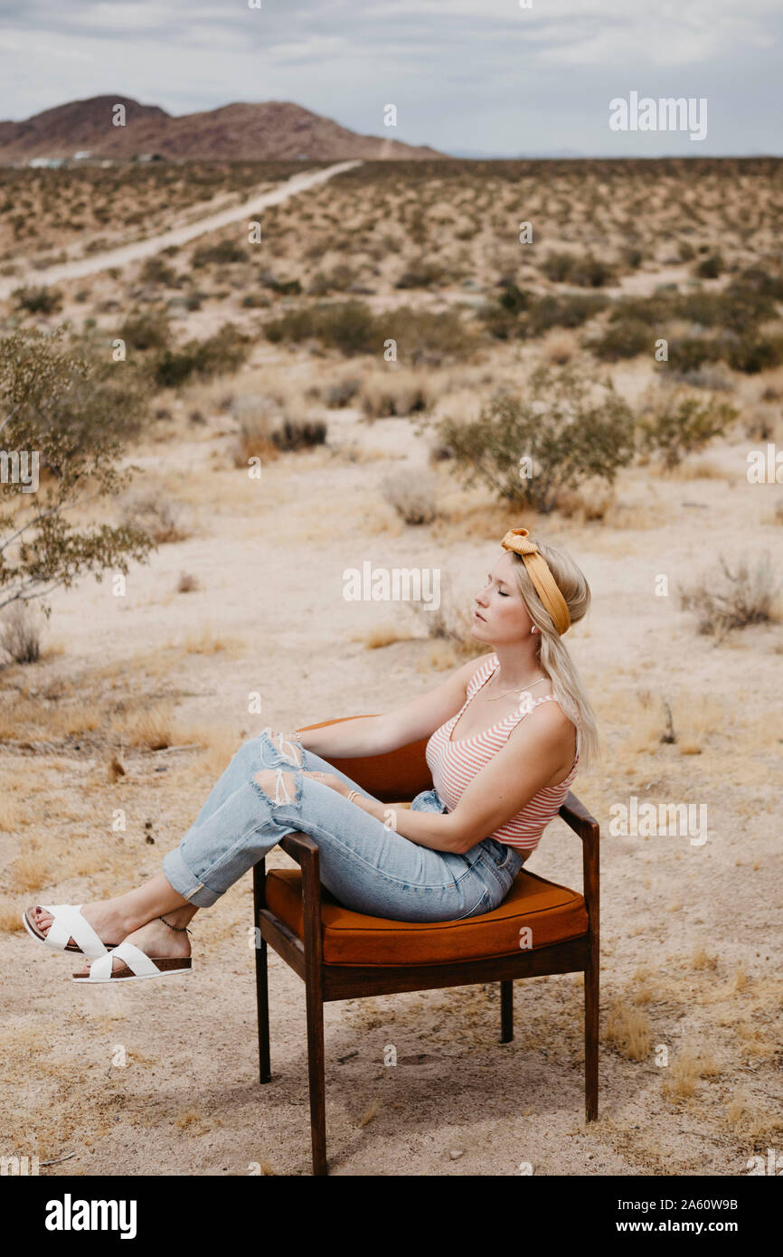 Donna seduta su una sedia nel paesaggio del deserto, Joshua Tree National Park, California, Stati Uniti d'America Foto Stock
