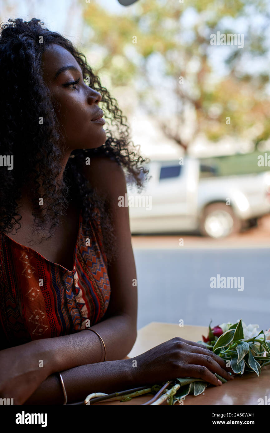 Ritratto di giovane donna africana con fiori sul tavolo in un cafe, guardando fuori della finestra Foto Stock