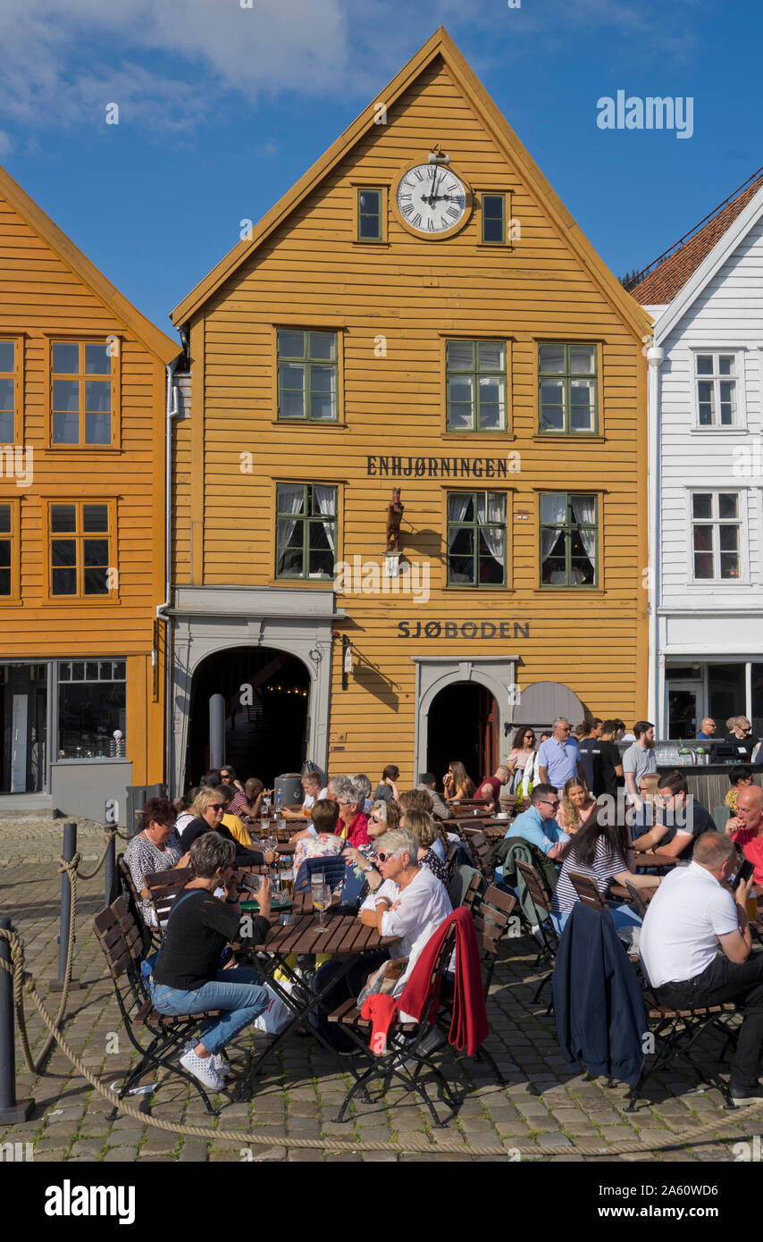 I turisti sedervi al sole in outdoor bar e caffetterie nel molo vecchio e tradizionali edifici in legno a Bryggen trimestre di Bergen, Norvegia Foto Stock