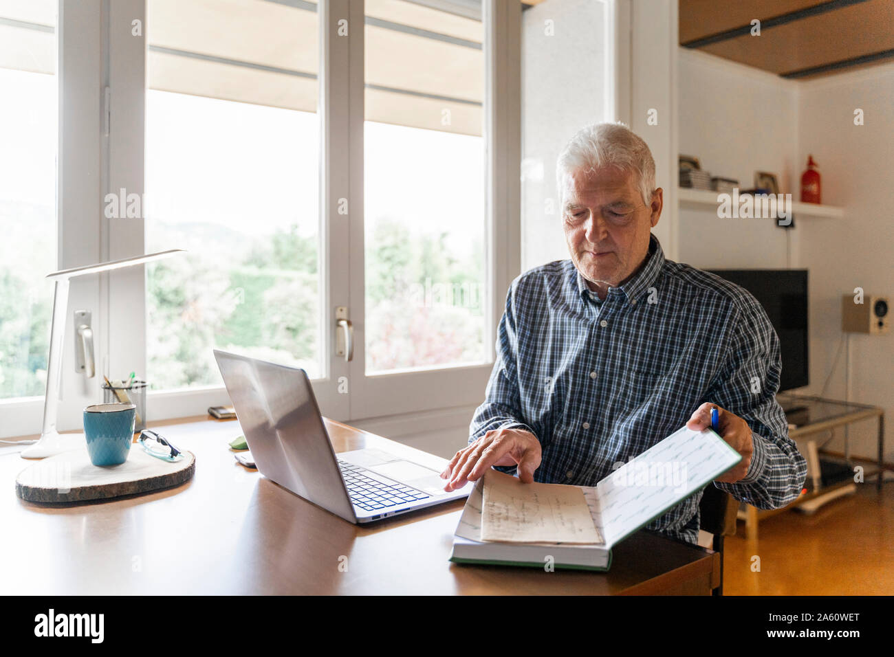 Senior uomo seduto a casa nella parte anteriore del computer portatile girando le pagine nel notebook Foto Stock