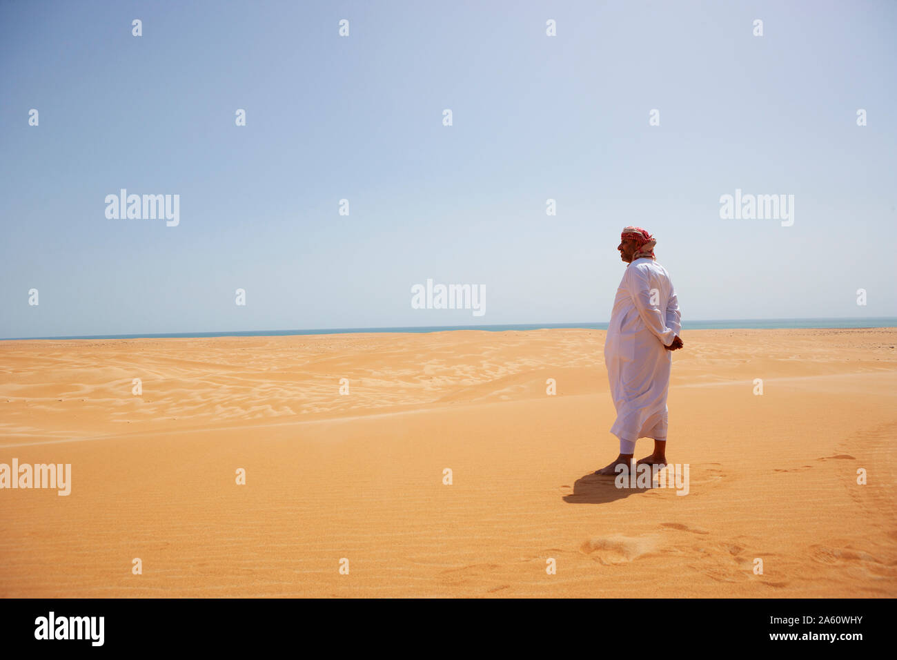 Bedouin in abito nazionale in piedi nel deserto, vista posteriore, Wahiba Sands, Oman Foto Stock