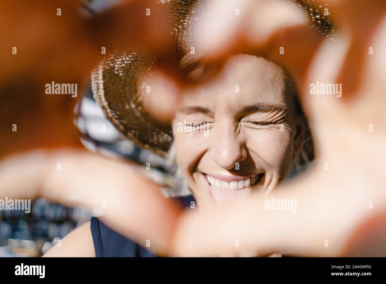 Donna con cappello di paglia, guardando verso il sole, rendendo a forma di cuore telaio del dito Foto Stock