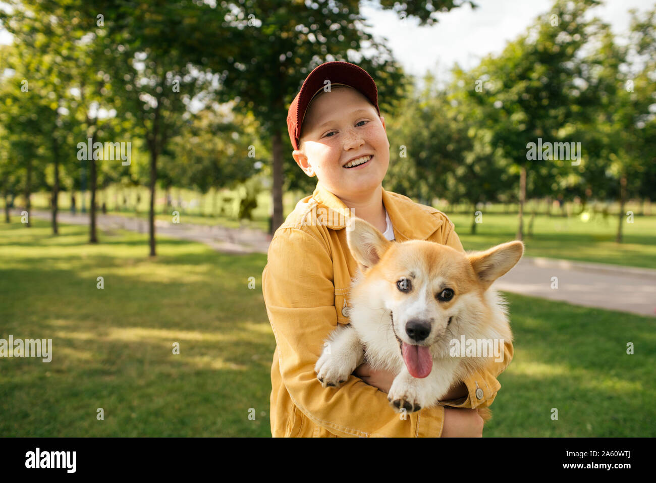 Ragazzo sorridente tenendo la sua Welsh Corgi Pembroke in un parco Foto Stock