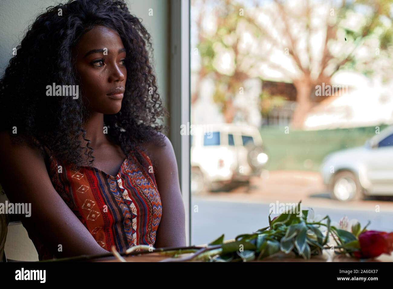 Ritratto di giovane donna africana con fiori sul tavolo in un cafe, guardando fuori della finestra Foto Stock
