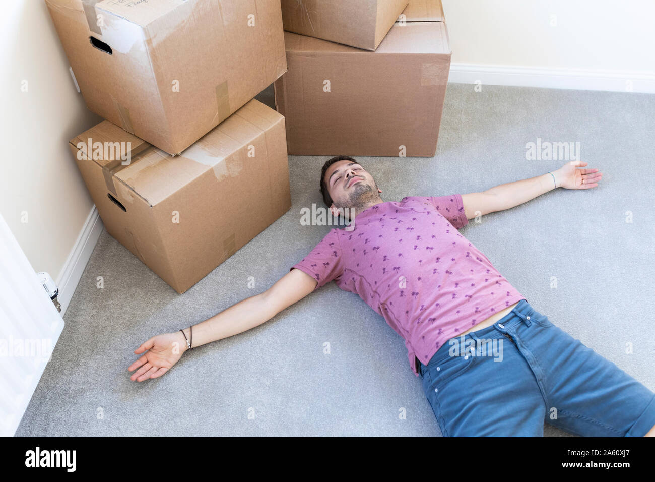 Stanco uomo disteso sul pavimento moquette nella nuova casa Foto Stock