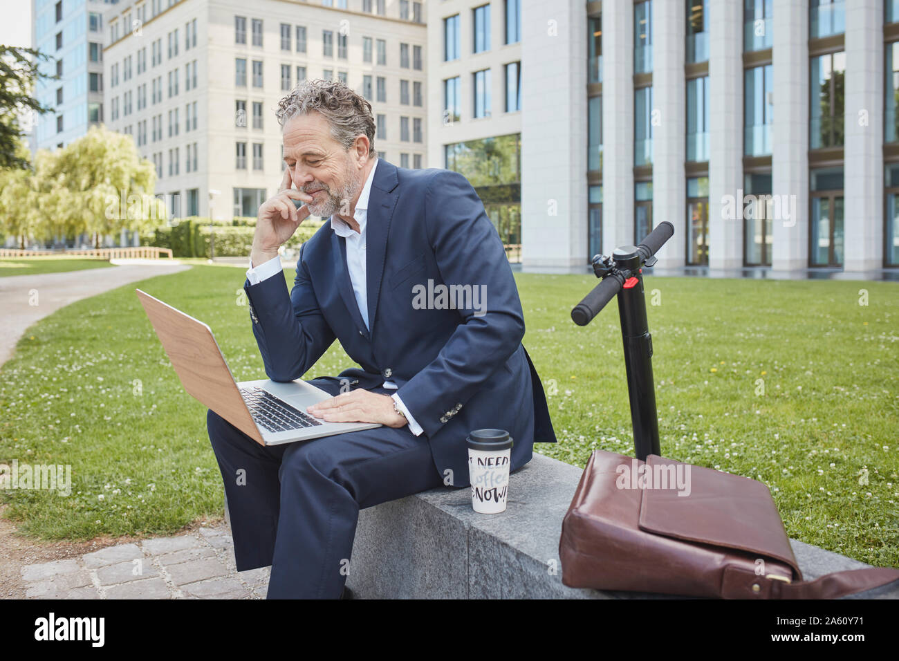 Imprenditore maturo seduto su di una parete della città utilizzando laptop Foto Stock