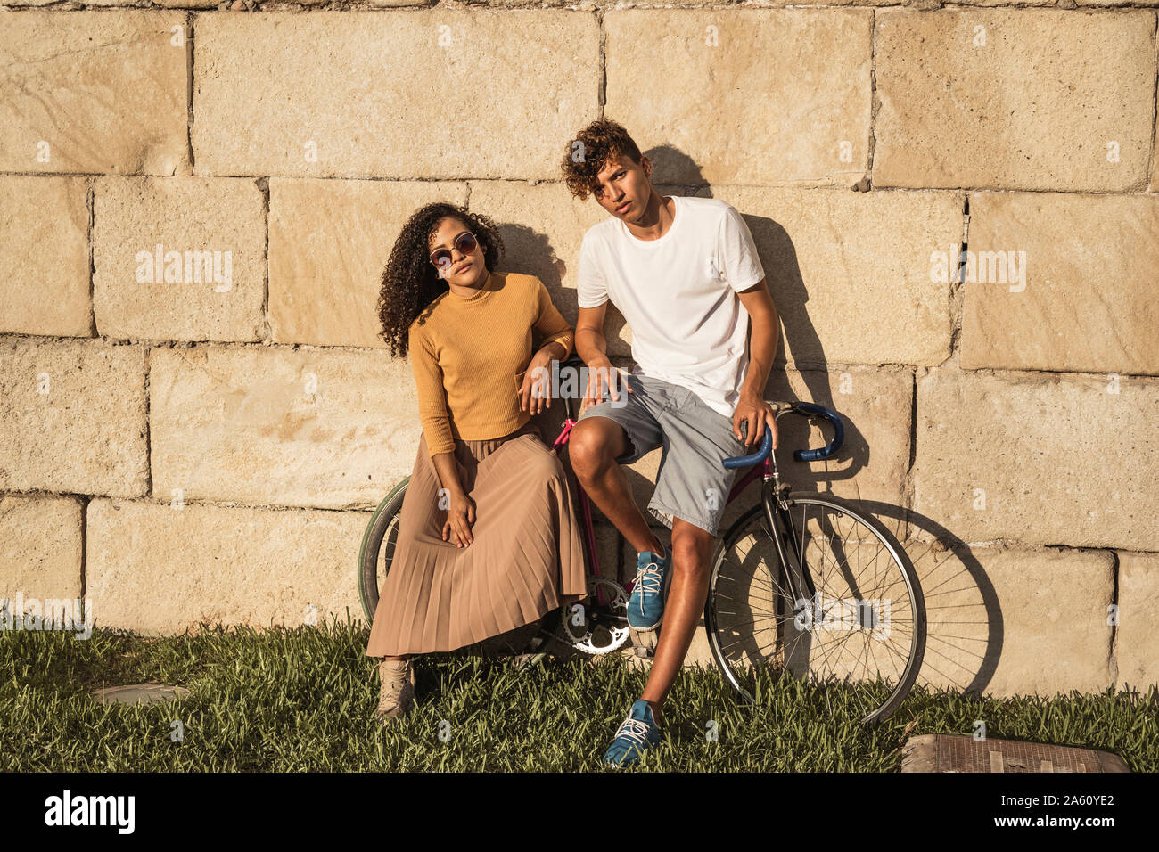 Coppia giovane con la bicicletta, appoggiata sul muro di pietra, alla moda Foto Stock