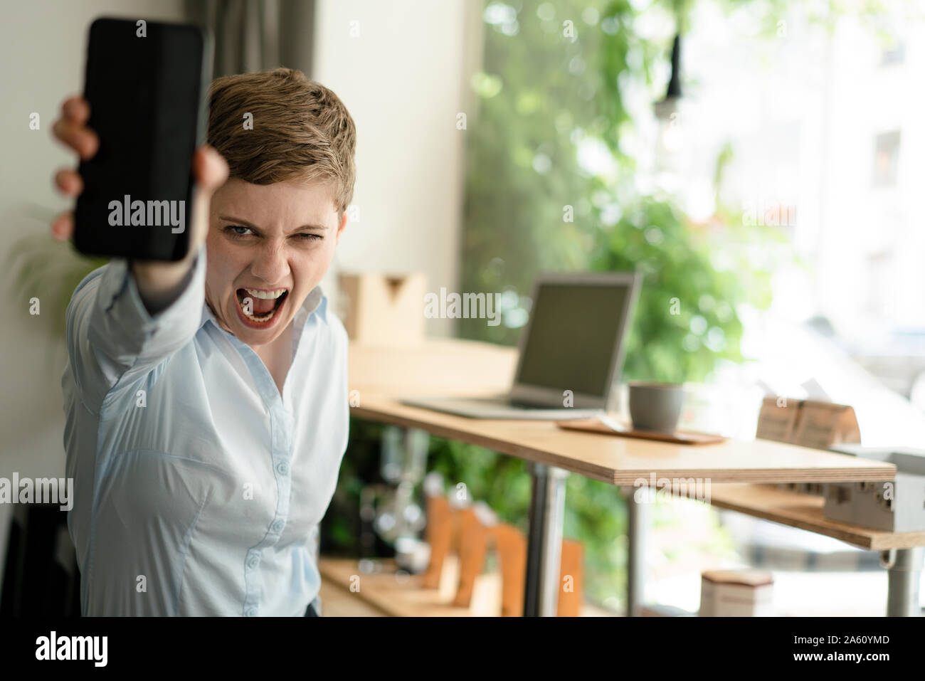 Ritratto di urlando imprenditrice tenendo il cellulare in un cafe Foto Stock