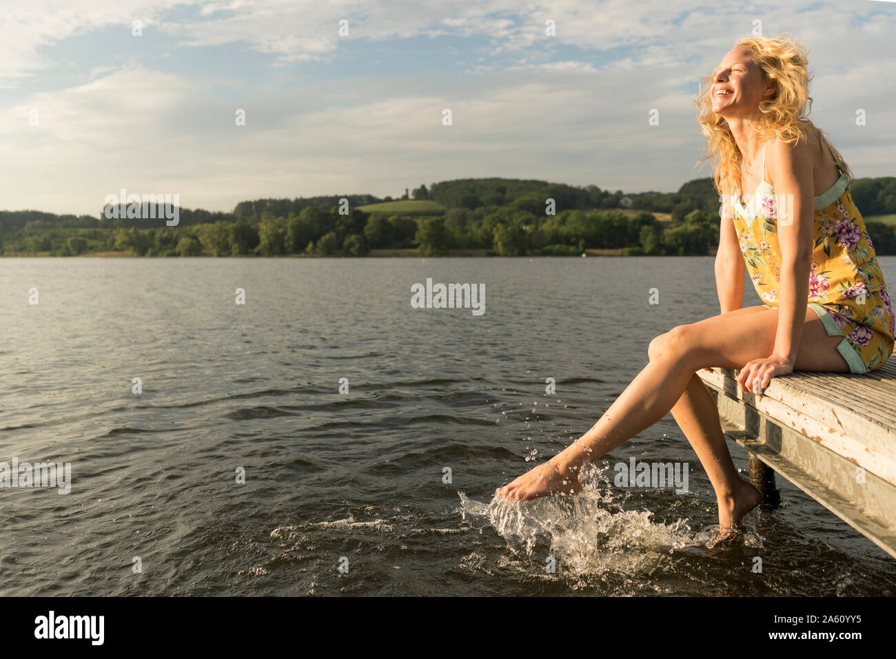 Giovane donna seduta su un molo a un lago con i piedi in acqua Foto Stock