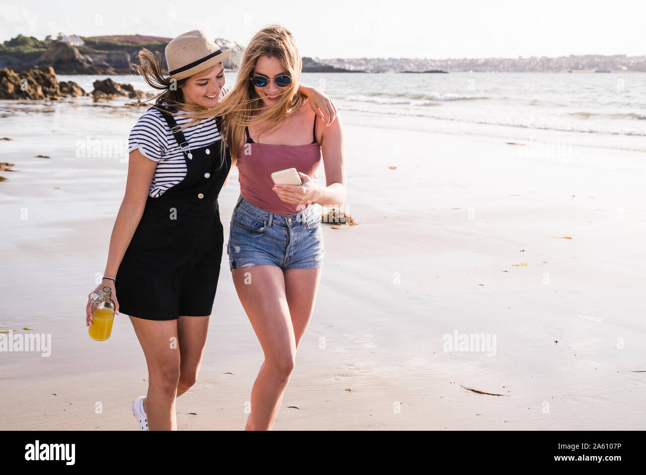 Due amiche divertendosi, passeggiate sulla spiaggia, tenendo selfies dello smartphone Foto Stock