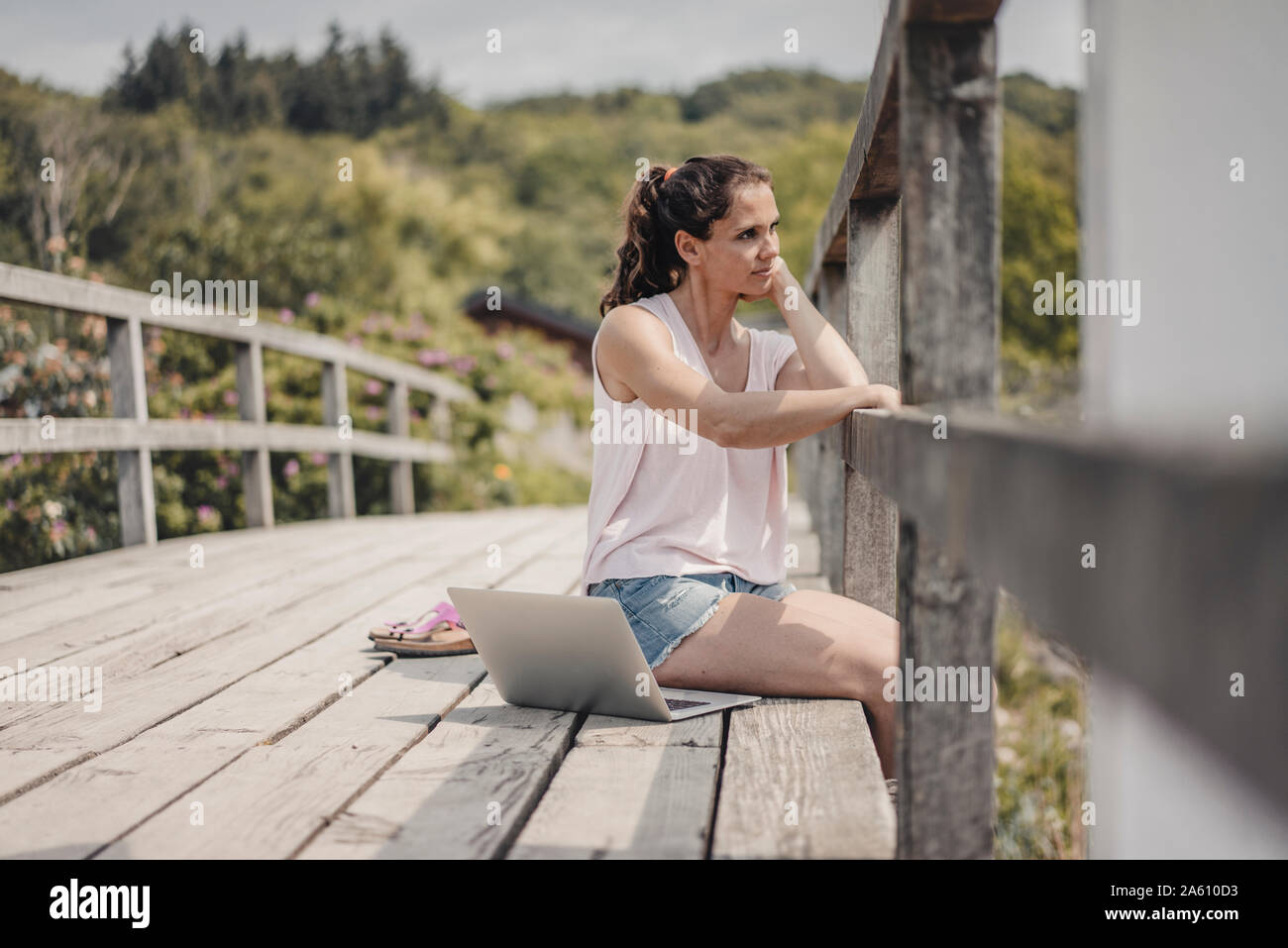 Donna con notebook seduto sul ponte di legno, guardando a vista Foto Stock