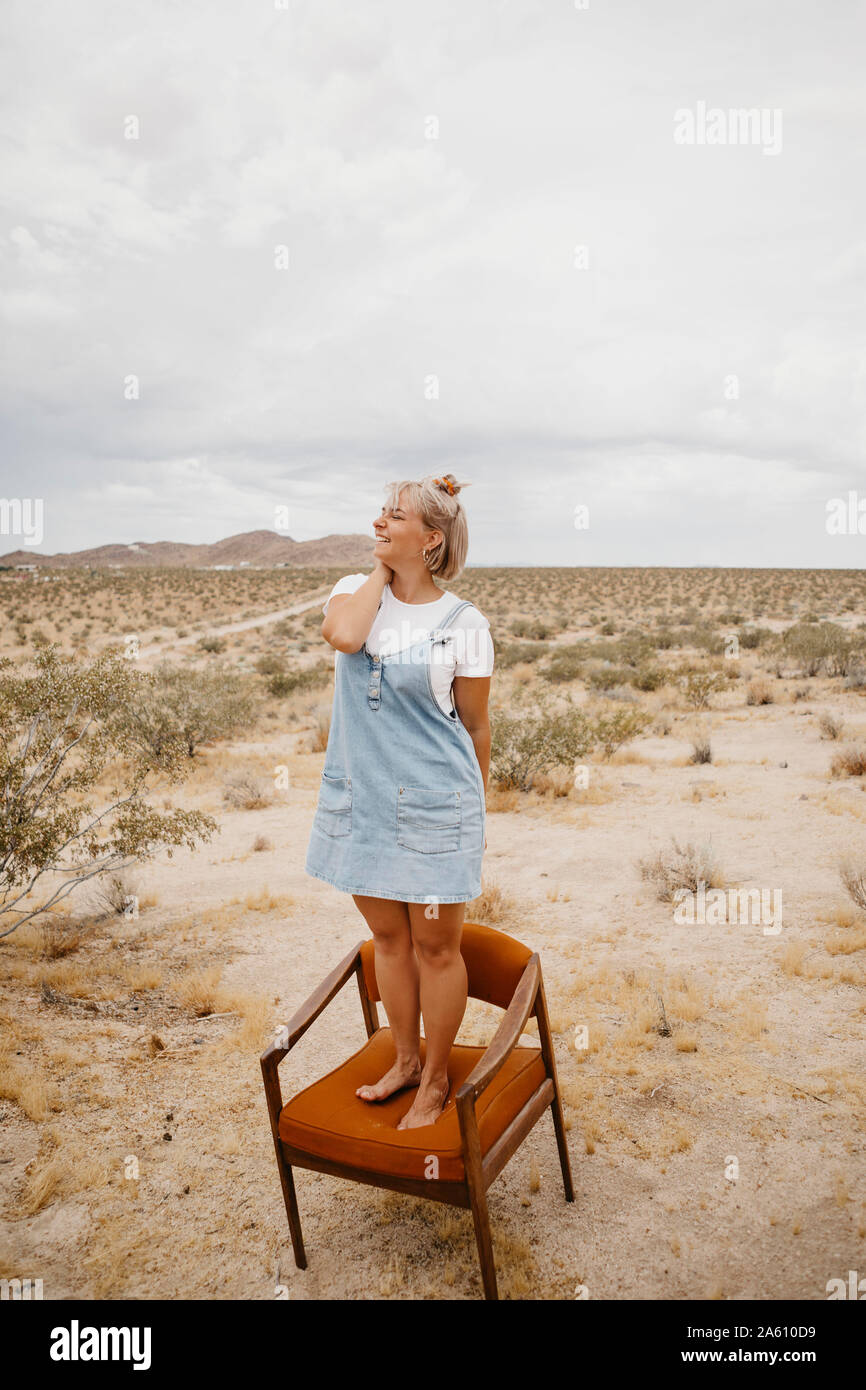 Donna in piedi su una sedia nel paesaggio del deserto, Joshua Tree National Park, California, Stati Uniti d'America Foto Stock