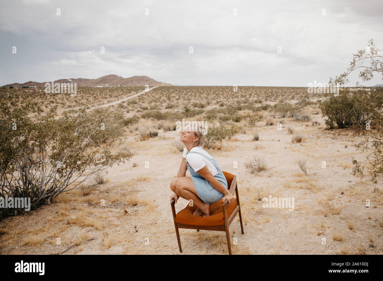 Donna accovacciata su una sedia nel paesaggio del deserto, Joshua Tree National Park, California, Stati Uniti d'America Foto Stock