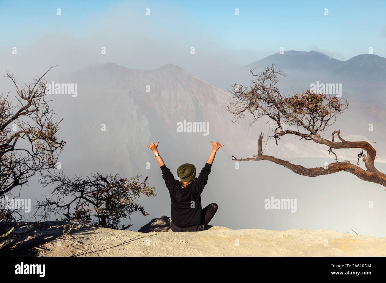 Donna con maschera respiratore seduti al vulcano Ijen e alzando le braccia, Java, Indonesia Foto Stock