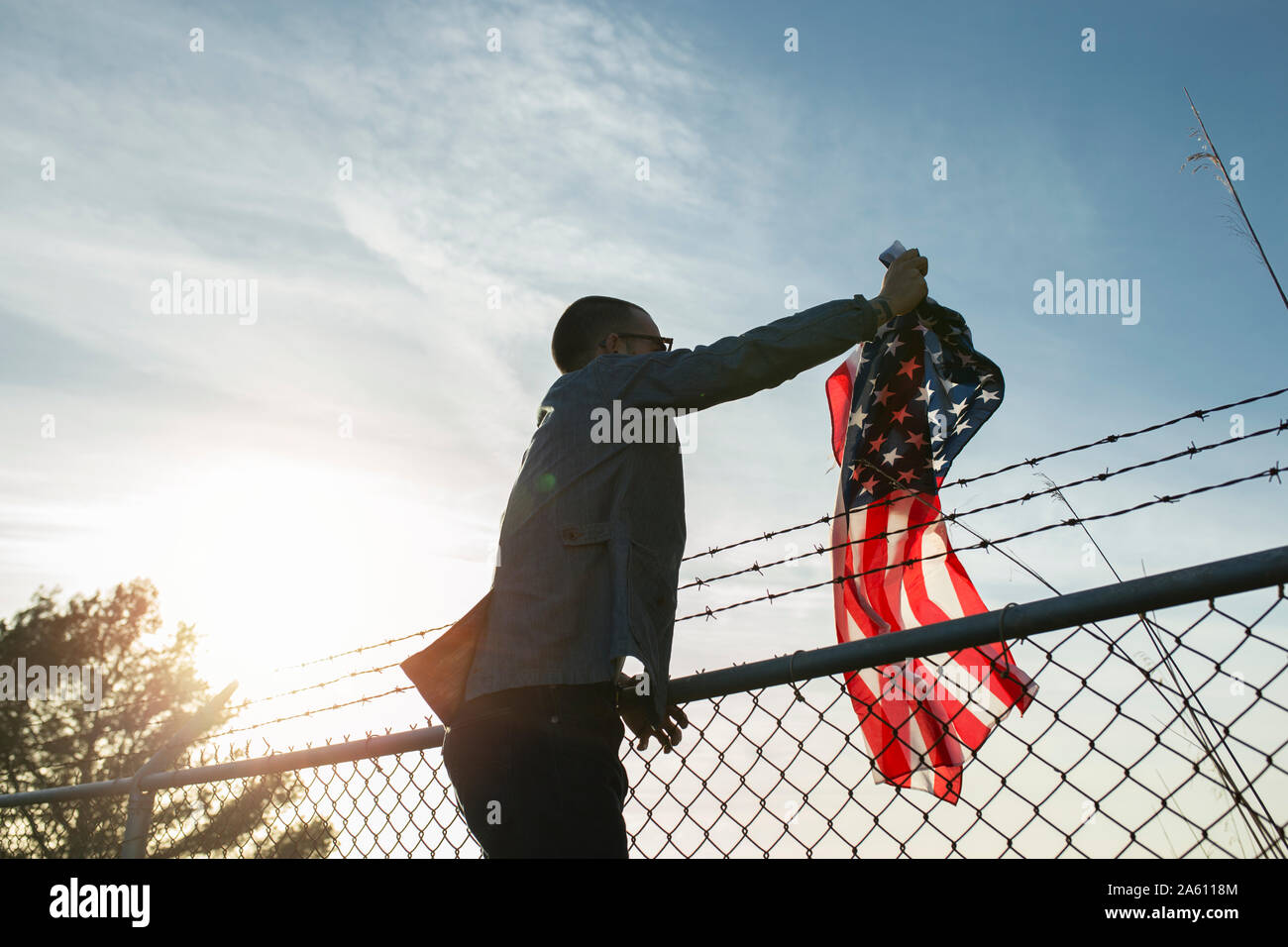 Giovane uomo rimozione US-bandiera americana da brabed recinto di filo Foto Stock