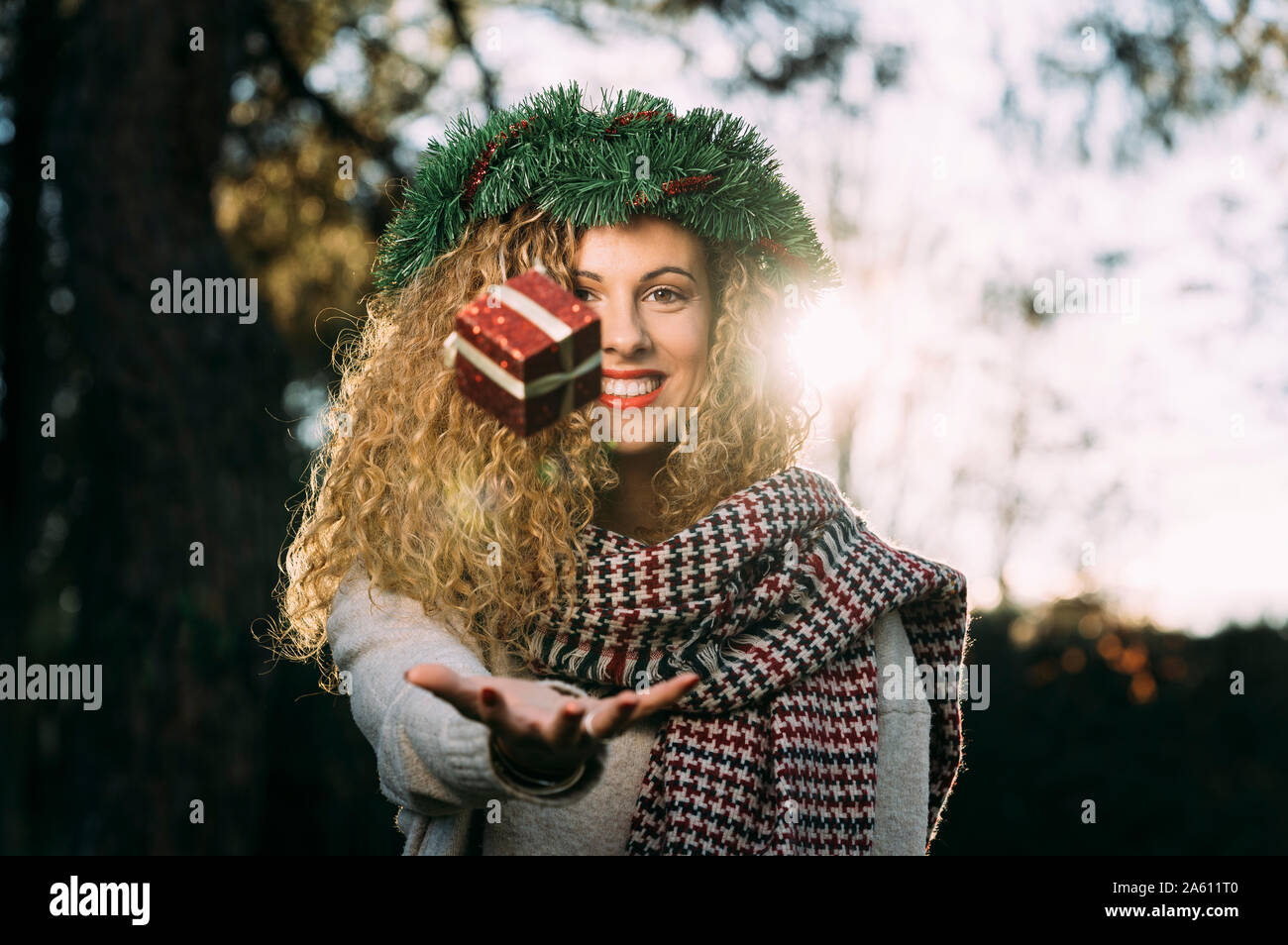 Ritratto di sorridente giovane donna con la ghirlanda di Natale sul suo capo la giocoleria con il regalo di Natale Foto Stock
