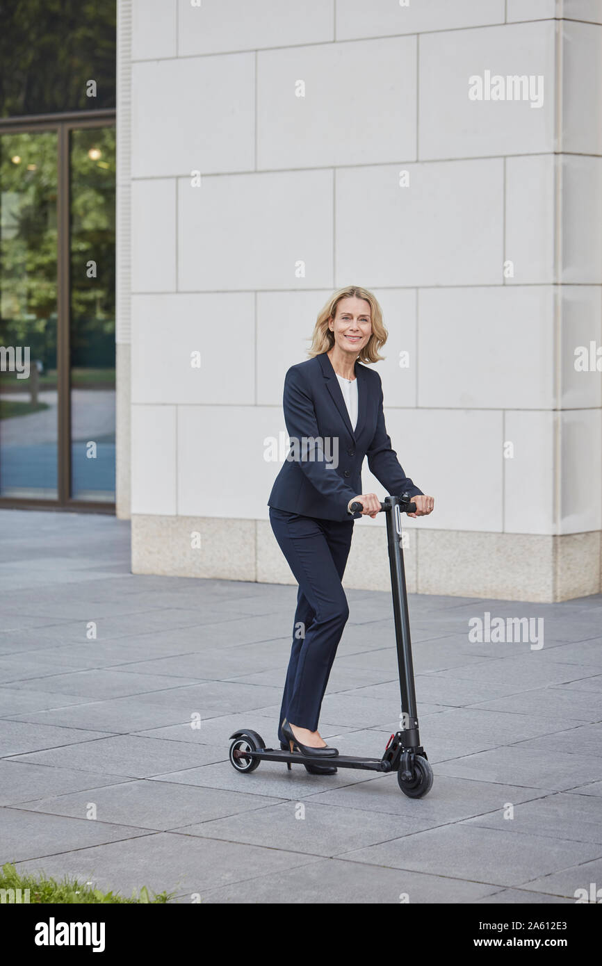 Imprenditrice sull'e-scooter stnading prima di edificio per uffici in città Foto Stock