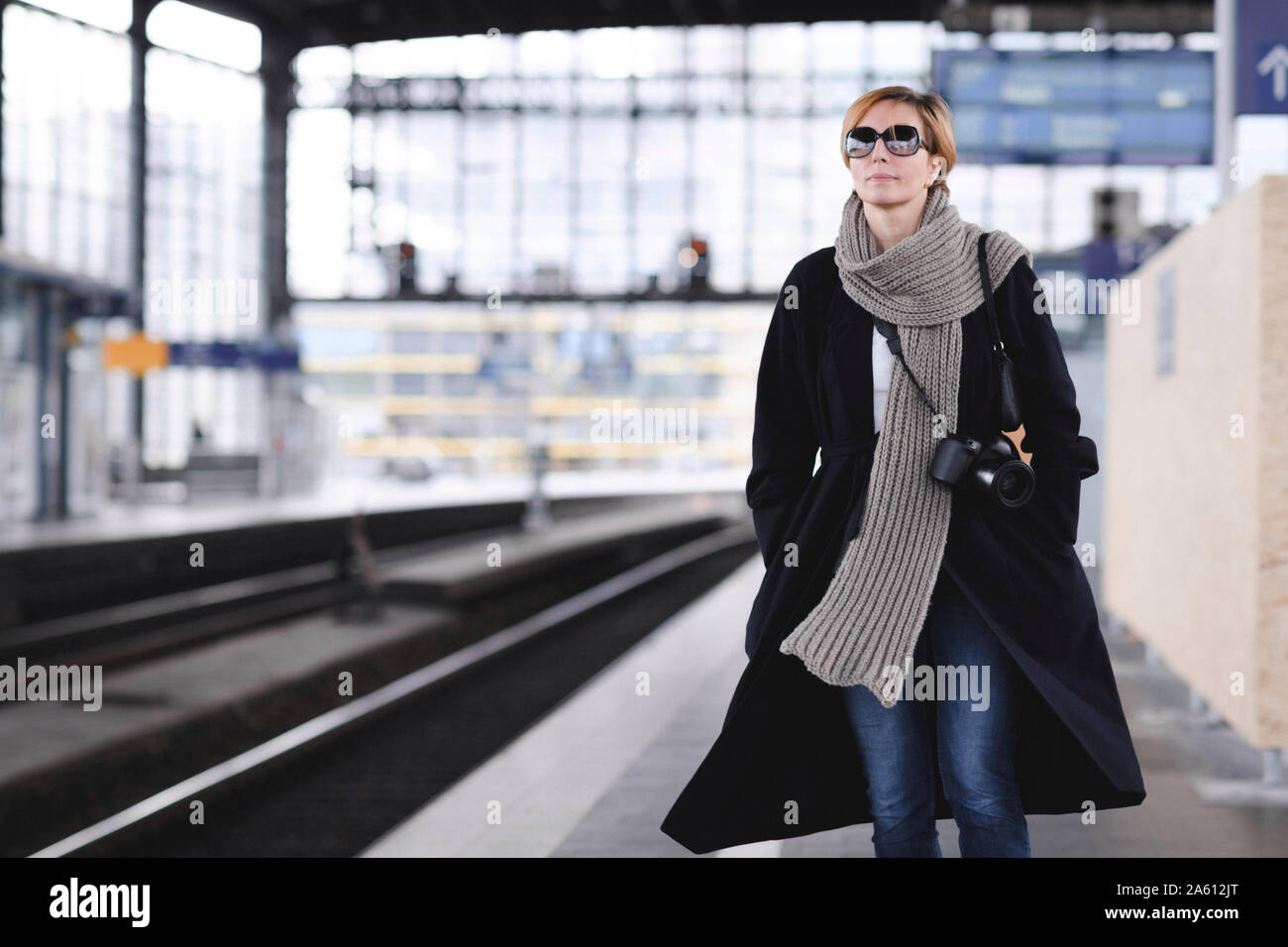 Donna matura con fotocamera vestita di nero e il cappotto di lana grande sciarpa in attesa in corrispondenza della piattaforma Foto Stock