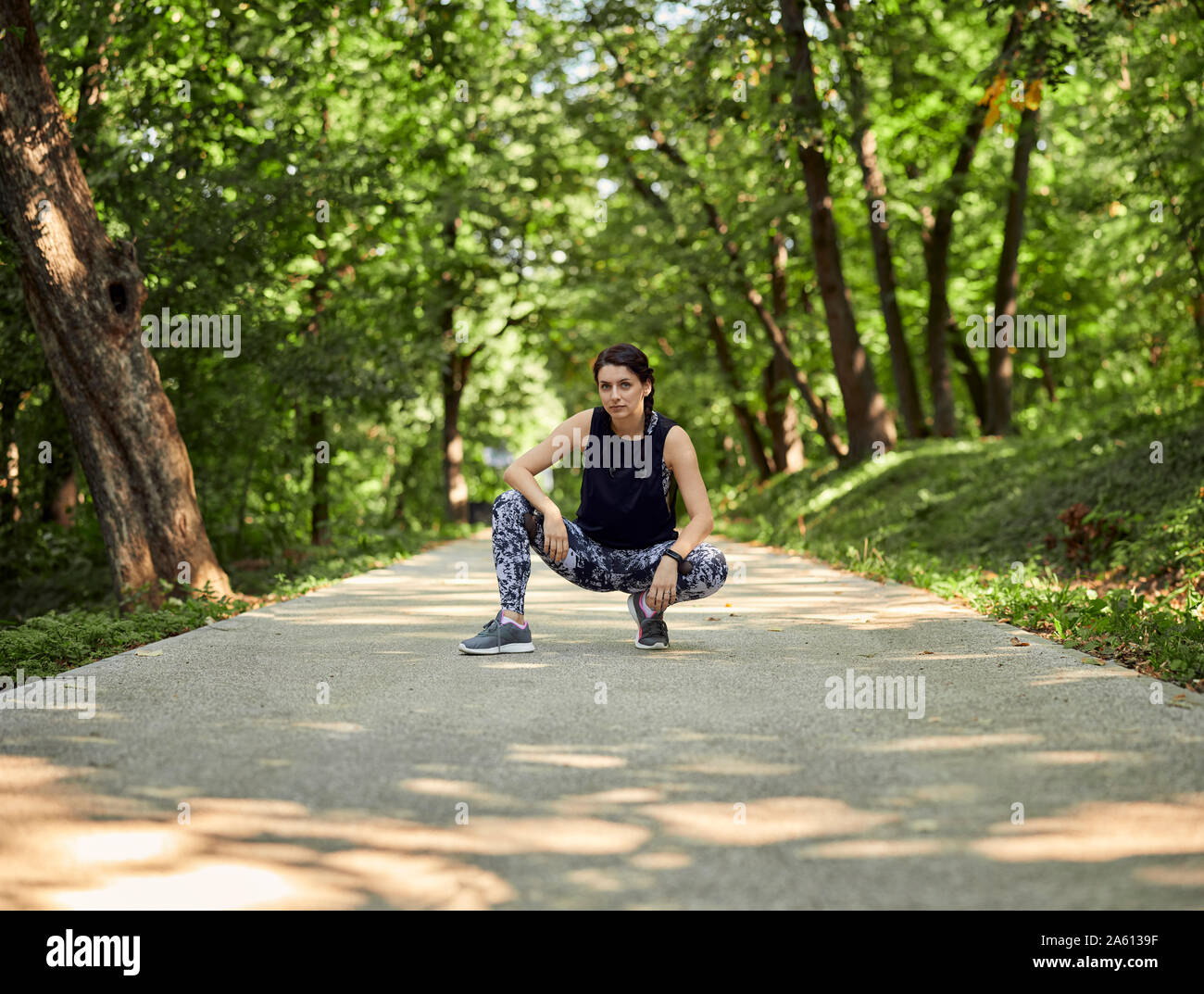 Ritratto di giovane sportivo donna accovacciata sul sentiero forestale Foto Stock