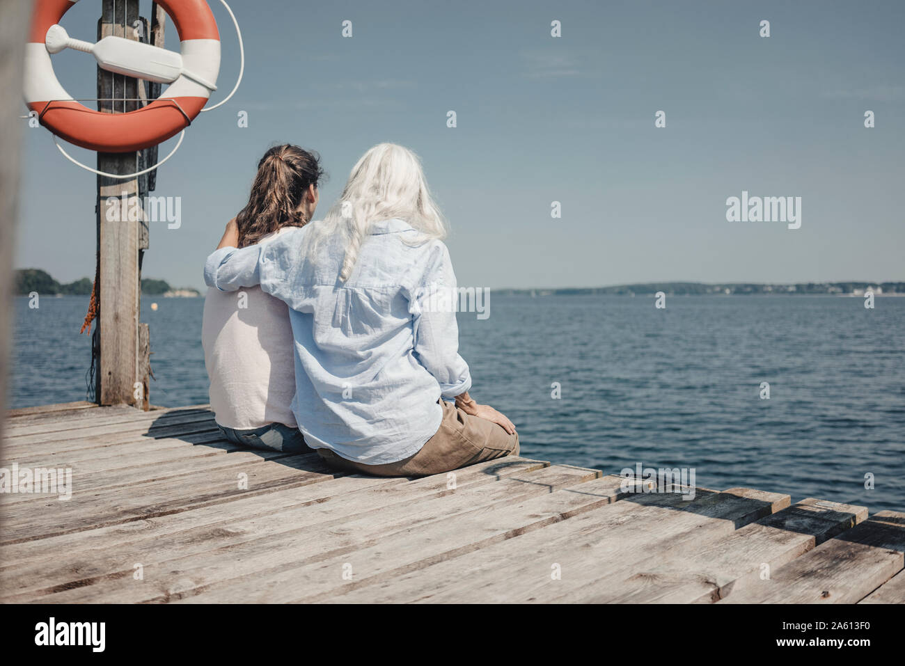 Madre e figlia guardando il mare seduti sul molo, vista posteriore Foto Stock