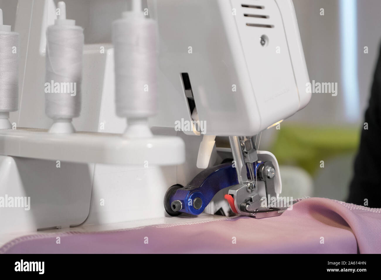 Trasformazione del tessuto del lembo di tessuto. Sarta lavorando a macchina per cucire rendendo maglie cuciture con maglia diritta su porpora, mani closeup. Sartoria abbigliamento Fabbricazione di business. Foto Stock