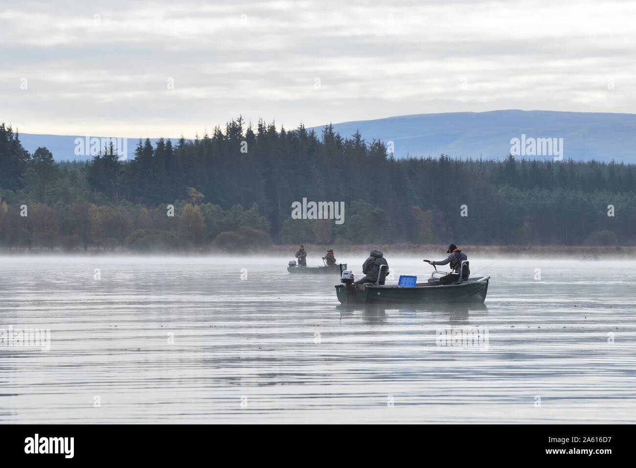 Un pescatore su una barca atterra un pesce in una fredda mattina d'autunno nebbiosa sul lago di Menteith pescando in Scozia, Regno Unito, Europa Foto Stock