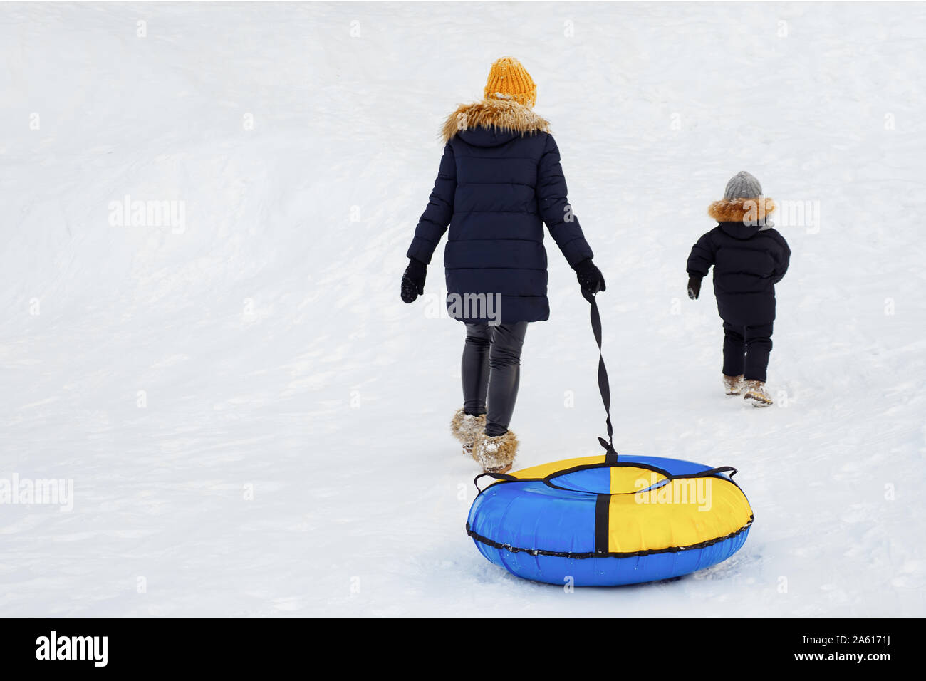 Vista posteriore della madre e figlio andare in salita con snow tube, copyspace Foto Stock