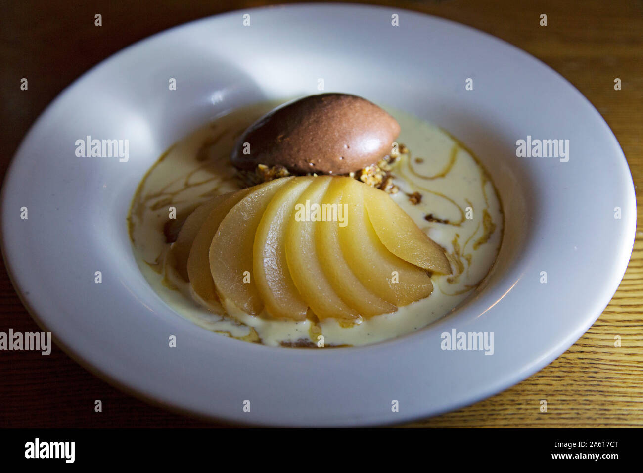 Un dessert di pera affogata con caramello gelato. Il piatto viene servito con una salsa cremosa. Foto Stock
