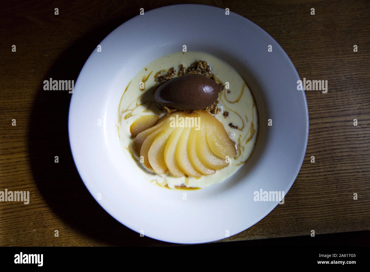 Un dessert di pera affogata con caramello gelato. Il piatto viene servito con una salsa cremosa. Foto Stock
