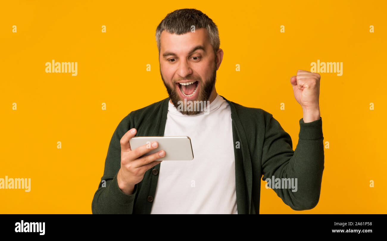 Emotivo uomo barbuto tenendo lo smartphone e il pugno di aggraffaggio Foto Stock
