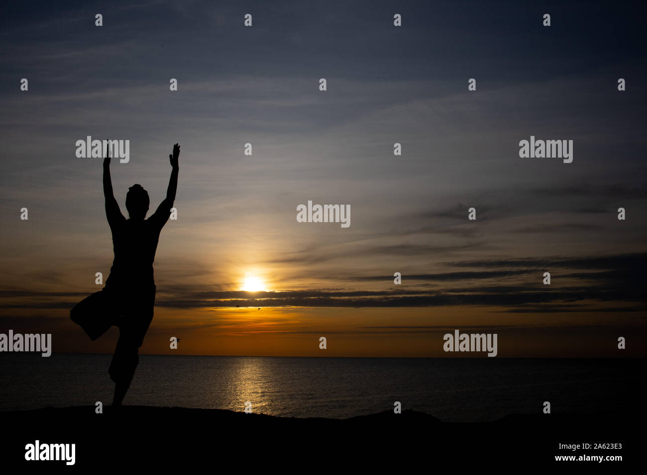 Silhouette di donna al tramonto, posizione di yoga contro il sole al tramonto sull'isola di Bornholm, Danimarca, lo Yoga al tramonto sull'isola Foto Stock