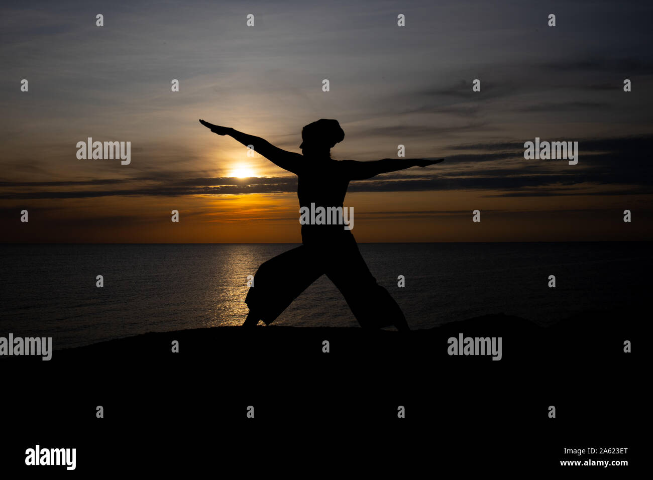 Silhouette di donna al tramonto, posizione di yoga contro il sole al tramonto sull'isola di Bornholm, Danimarca, lo Yoga al tramonto sull'isola Foto Stock