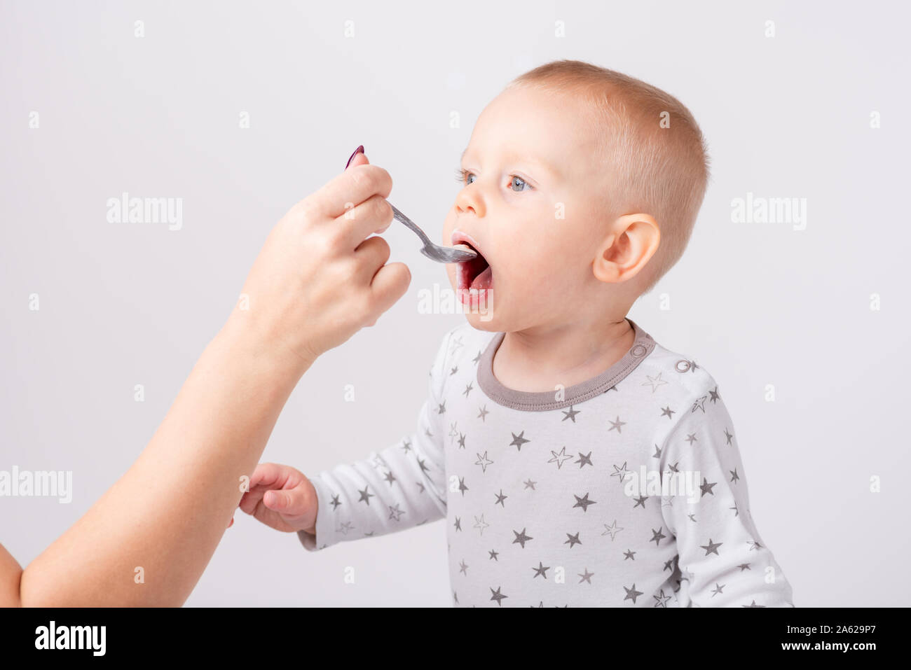 Mom alimenta la sua gioiosa bambino. lei tiene un cucchiaio vicino a bocca aperta di un bambino. Una faccia sporca dal cibo. Isolato sullo sfondo bianco. Copia dello spazio. Foto Stock