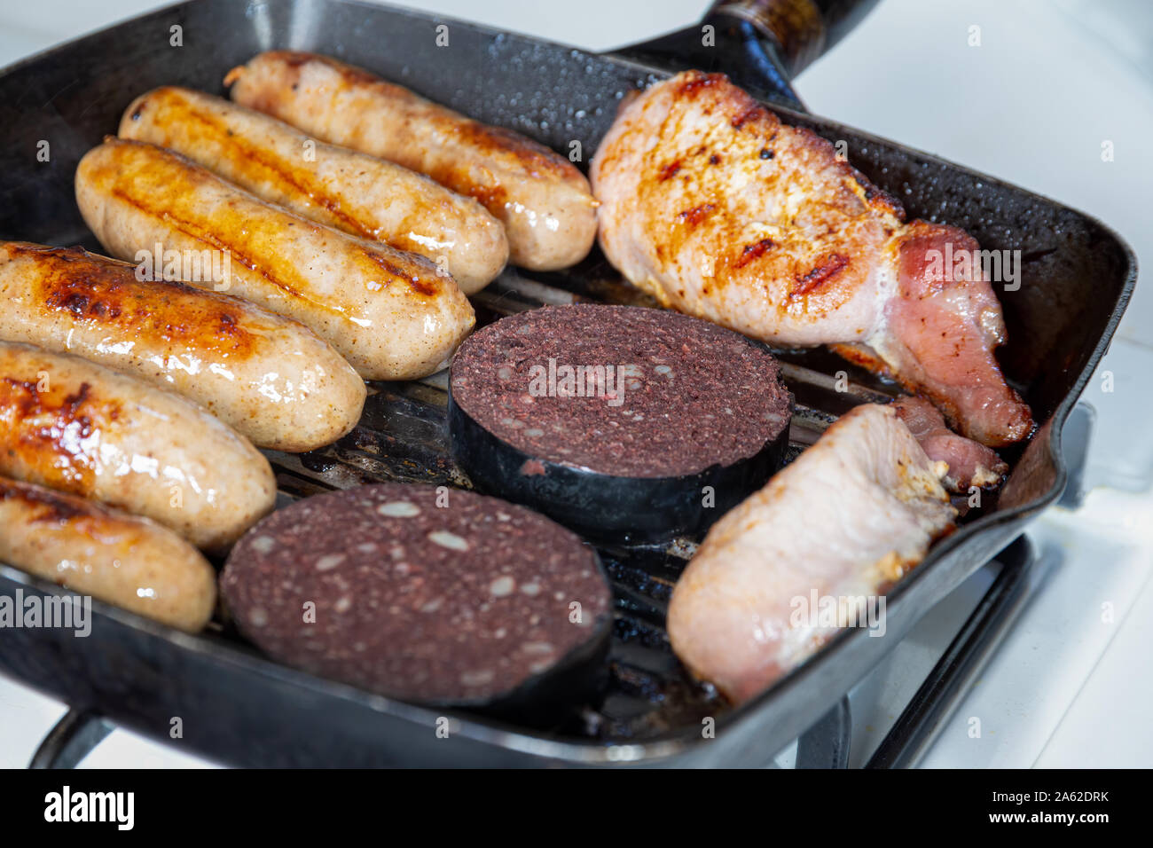 Salsicce Cumberland, back bacon e black pudding la cottura in una piastra pan Foto Stock