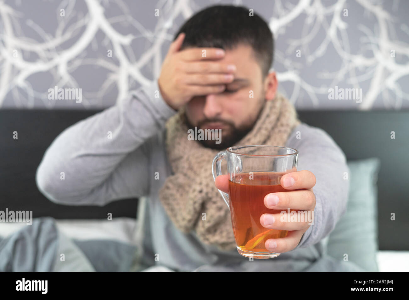 Malattia. Allegria a casa. Un giovane uomo è malato, viene trattata a casa. Tè nero con il limone in una tazza trasparente in una mano d'uomo. Infezione, epidemia, bacil Foto Stock